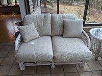 Front view of white-painted rattan loveseat with beige patterned cushions and two throw pillows showing overall condition and style.