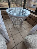 Rattan side table with a glass top, showing weathered white paint and lattice rattan base, viewed from the side.