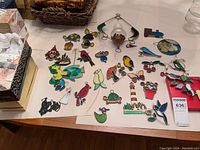 Full view of all the sun catchers laid out on a table, showing diverse designs including birds, turtles, lighthouse, flower pot, and a small train figure.