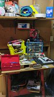 Photo showing a workbench with various hardware storage boxes filled with screws, nails, and parts, yellow parts organizer, and other tools scattered around the bench.