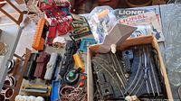Photo of Lionel electric train parts including multiple train cars, track sections, transformer box, wiring, and accessories on a table in a garage.