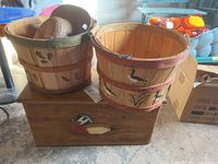 Photo of wooden trunk with painted duck and apple baskets with painted floral and duck designs holding three straw hats