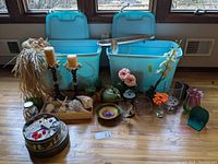 Wide view of lot contents spread out on wooden floor showing two blue bins open and arranged with flowers, vases, candles and decor