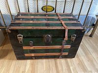 Closed view of vintage steamer trunk showing black and green panels with leather straps and metal latches.