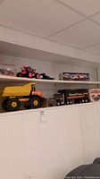 Shelf view showing multiple vintage toy trucks including a large yellow Tonka dump truck, NYLint Overnight Express tractor trailer, toy dune buggies, and other toys.