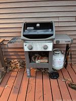 Full front view showing Weber Spirit II grill with propane tank and barbecue utensils hanging on side hooks.
