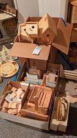 View showing two boxy wooden birdhouses with simple entry holes and perches, surrounded by additional craft pieces in boxes.