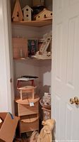 Wood crafts stored on basement shelving including various unpainted wood birdhouses, small craft tables, and decorative wooden items.