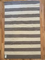 Photo of rectangular two tone grey and off-white striped area rug laying flat on hardwood floor, clearly showing stripe pattern and size.