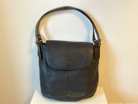 Front view of the Cledran black leather handbag, showing flap closure with embossed logo and shoulder strap.