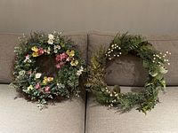Two decorative hanging wreaths placed on a beige couch, showing the colorful floral wreath on the left and the gold and green winter wreath on the right.