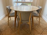 Four grey upholstered chairs arranged around a round white table in a tiled breakfast nook