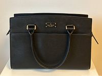 Front view showing gold-tone logo plate and rolled handles