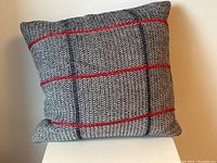 Front view of grey pillow with red and black stripes on a knit fabric, placed against a white background.