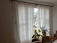 Two off-white linen curtain panels hanging on a black wrought iron rod in front of a window