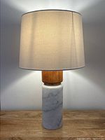 Front view of the lamp illuminated showing shade, teak neck, marble base