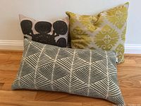 Three modern decorative pillows: rectangular gray striped pillow in front, square yellow patterned and black floral patterned pillows in back on hardwood floor.