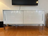 Front view of the white credenza cabinet with left sliding door closed and right door partially open, showing chrome legs and handles.