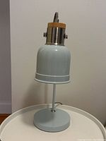 Full view of blue desk lamp showing the shade looking downward on a round white surface with beige wall background.