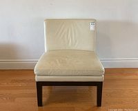 Front view of cream leather modern chair with dark wood legs against a wall on hardwood floor.