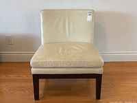 Front view of the West Elm leather chair showing cream colored leather seat and backrest with brown wood legs. Chair is positioned against a white wall and wooden floor.