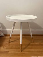 Front view of the white round side table showing the tray-top and three legs with wood finishes at the bottom.