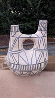 Front view of Anthropologie geometric ceramic vase showing cream color and blue/tan geometric patterns with two spouts and a circular center opening