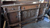 Full view of antique wooden buffet showing front side with three drawers, two cupboards, and carved columns and floral decorations.