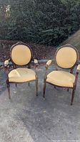 Front view of two antique armchairs showing light yellow upholstery with stain visible on left chair seat and carved wood frames.