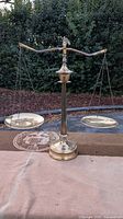 Full view of the brass balance scale standing upright with two hanging round pans on either side.