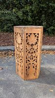 Full view of hexagonal carved wood pedestal showing intricate floral and leaf design on the side panels.