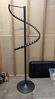 Full view of the black metal spiral clothing rack showing the stand and circular base.