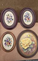 Four oval framed floral art pieces including three embroidered pansies and one painted yellow rose