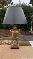 Front view of the large brass table lamp with black lampshade, showing the overall shape and color.