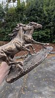 Side angle view of two running horses bronze statue held in hand, showing detailed features and flowing manes.