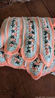 Folded crochet quilt showing scalloped edge detail in blue, peach, white, and green yarns.