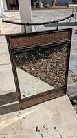 Full front view of vintage mirror with metal frame and rattan paneling showing reflective glass and top metal hanging bar.
