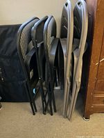 Side view of the assorted folding chairs stacked together showing black and light grey frames with fabric seats and backs.