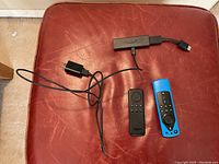Amazon Fire TV Stick with two remote controls and power adapter on red leather surface.