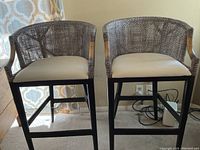 Pair of bar stools shown side by side in natural light, highlighting woven wicker back and light upholstery