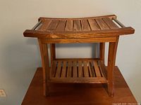 Wooden shower bench with slatted wood design and metal support bars on sides, visible wear on wood surfaces.