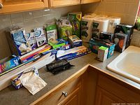 Photo of kitchen counter with consumable paper products including Bounty paper towels, plastic forks, sandwich bags, aluminum foil, plastic wrap, and lightbulb packages.