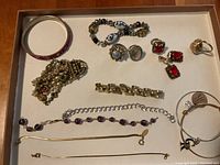 Overview of the lot showing various costume jewelry rings, bracelets, and a pair of earrings arranged in a box against a brown background