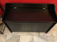 Front view of dark brown entryway storage bench closed, showing paneled front and slightly curved sides.
