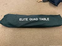 Dark green carrying case labeled 'ELITE QUAD TABLE' storing the folded camping table.