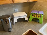 Kitchen countertop with two step stools and a small chrome pedal trash can.