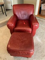 Front view of red leather armchair with matching ottoman placed in front, showing overall shape, structure, and upholstery condition.