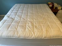View of padded queen mattress topper showing quilted rectangular pattern and smooth laying on mattress