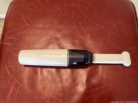 Portable vacuum cleaner with the brush attachment extended, shown on a leather surface.