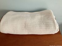 Folded white textured cotton blanket with visible weave detail, placed on wooden surface.